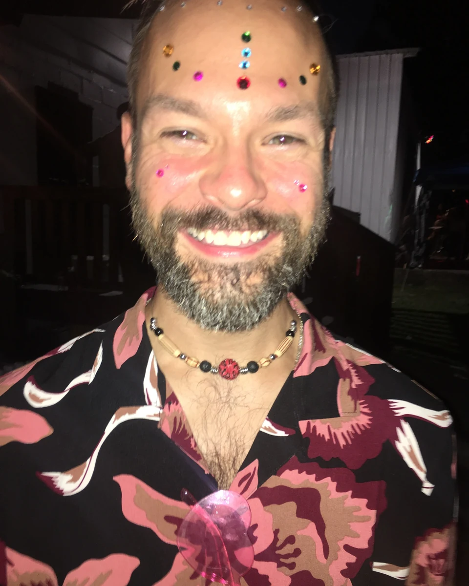 Joseph Malicke, laughing, with bright gems across his forehead, in a floral shirt